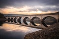 Long arched bridge crossing Ladybower reservoir reflected in Derwent Valley still deep river water with dramatic sunrise beautiful