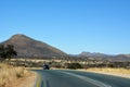 A long asphalt road in the desert in perspective against a blue sky. A car drives in the distance along the road Royalty Free Stock Photo