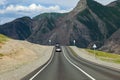 A long asphalt road with a white dividing strip against the backdrop of high mountains with cars riding on a clear warm summer day