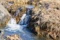 Long-awaited spring creeks flow over ravines and hills on a sunny day. Water rapids and waterfalls of streams among the dry grass Royalty Free Stock Photo
