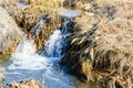 Long-awaited spring creeks flow over ravines and hills on a sunny day. Water rapids and waterfalls of streams among the dry grass Royalty Free Stock Photo