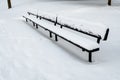 Long black metal sports spectator bench covered in snow on a snowy field