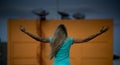 With long blonde hair stands with his back to the camera with raised arms on background of orange walls with large