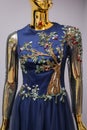 Long, blue designer, evening, women`s dress handmade on gold, glossy mannequin. With white and gold ornament in