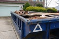 Long blue dumpster full of wood and other debris in the driveway in front of a house in the suburbs Royalty Free Stock Photo