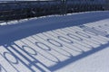 Long blue shadows on the white snow from the metal wrought iron fence on a sunny winter day. Abstraction. Background. Royalty Free Stock Photo