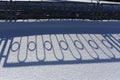 Long blue shadows on the white snow from the metal wrought iron fence on a sunny winter day. Abstraction. Background. Royalty Free Stock Photo