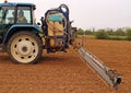 Long boom sprayer, trailed by a tractor, prepares to spray pesticides on a field with sprouts