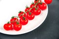 Long branch of organic ripe fresh cherry tomatoes on a white plate laying on black texture background. Royalty Free Stock Photo