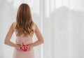 A long brown hair female wearing pink sleeveless dress stand hiding red gift box with white ribbon behind her back Royalty Free Stock Photo