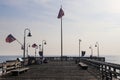 A long brown wooden pier with American flags flying from curved light posts and benches along the edge of the pier Royalty Free Stock Photo