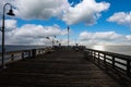 A long brown wooden pier with American flags flying on curved light posts with people walking and fishing on the pier Royalty Free Stock Photo