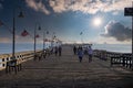 A long brown wooden pier with American flags flying on curved light posts with people walking and fishing on the pier Royalty Free Stock Photo