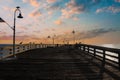 A long brown wooden pier with American flags flying on curved light posts with people walking and fishing on the pier Royalty Free Stock Photo