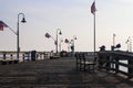 A long brown wooden pier with American flags flying on curved light posts with people walking and fishing on the pier Royalty Free Stock Photo