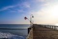 A long brown wooden pier with American flags flying on curved light posts with people walking and fishing on the pier Royalty Free Stock Photo