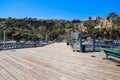 A long brown wooden pier with tall gray and red lamp posts along the pier with green benches and beach front homes Royalty Free Stock Photo