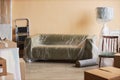 Long comfortable soft couch covered with cellophane standing by wall