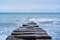 Waves break on rocks and fly apart into small drops and turn into foam. Long concrete breakwater stretching away into depths of