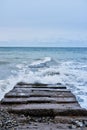 Waves break on rocks and fly apart into small drops and turn into foam. Long concrete breakwater stretching away into depths of