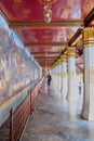 A long corridor decorated with wall paintings. Part of a Buddhist temple. A man goes into