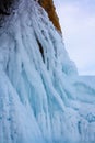 Long curved icicles melted in the sun hang on a rock.