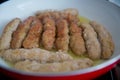 The long cutlet is fried in a red pan. She cooks the cutlet in a white pan