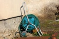 Long dark green garden hose mounted on garden hose reel with small wheels for easier transfer left in family house backyard