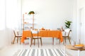 Long dining room table covered with orange tablecloth and comfortable white chairs Royalty Free Stock Photo