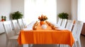 Long dining room table covered with orange tablecloth and comfortable white chairs around it Royalty Free Stock Photo