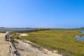 A long dirt footpath surrounded by blue ocean water and lush green plants and grass with a metal fence Royalty Free Stock Photo