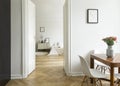 A long distance view from a dining room into a bedroom in a high ceiling flat. Monochromatic white interior with herringbone parqu