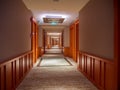 Long empty carpeted hallway / corridor in the interior of a hotel flanked by wooden doors Royalty Free Stock Photo