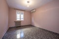 Long empty room with ugly dark tiled floor and pale pink painted walls, cast iron radiator under the window