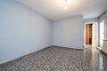 Long empty room with ugly dark tiled floors and pale soft blue painted walls, aluminum radiator and exit door to a terrace