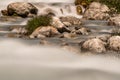 Long exposure and close-up detail of a river flowing between stones and clumps of grass. Royalty Free Stock Photo