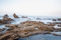 Long exposure fluffy ocean mists rush over tidal pool rocks at the beach Royalty Free Stock Photo