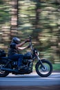 Long exposure of a motorcyclist riding past in the woods on a black Harley Davidson