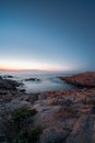 Long exposure photo of sea water washing jagged coastal rocks, Isola Rossa, Sardinia, Italy. Colourful sky after sunset Royalty Free Stock Photo