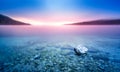 Long exposure of rock in lake at pebble beach with purple sunrise light.