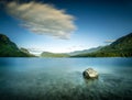 Long exposure of a rock in lake water at pebble beach.