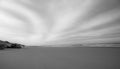 Long exposure of a rocky beach of Cap Ferret in France with a cloudy fan-shaped sky in black and white