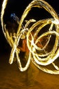 Long exposure shot from a fire juggling act, performed by a man with a red hat, showing the light trail create by the 3 burning