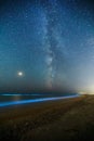 Long exposure shot of glowing plankton on sea surf and milky way. Blue bioluminescent glow of water under the starry sky