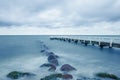 Long exposure shot of the sea with rocks and a pier on a cloudy day Royalty Free Stock Photo