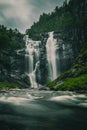 Long exposure shot of a Skjervefossen waterfall in a valley emerging from the forest in Bergen area