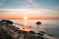 Long exposure of sunset over the ocean with beach and rocks in the forground