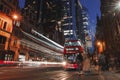 Long exposure of traffic lights with red bus on stop at the road. City buildings in the background at night