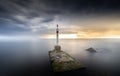 Long exposure view of a lighthouse on mossy rocky land in the sea under dramatic gray sky