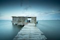 Long exposure view of a wooden pier lead to wooden hut on the water under dramatic gray sky Royalty Free Stock Photo